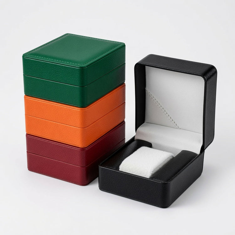 Stacked green, orange, and red single watch boxes beside an open black box with a white padded cushion.