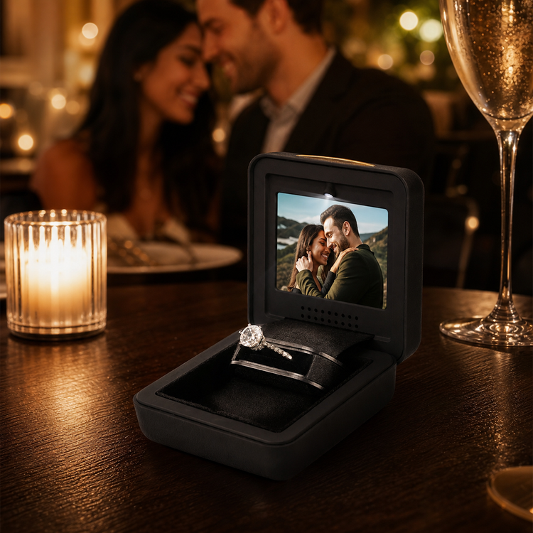 Open black video proposal ring box showing a couple on screen beside an engagement ring at a candlelit dinner