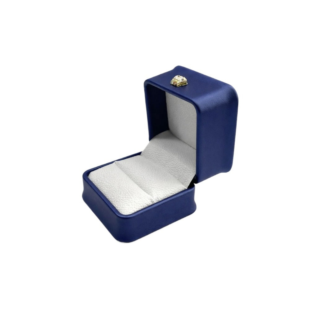 Open navy blue rounded-corner ring box with a light cushioned insert and gold-tone lid ornament.