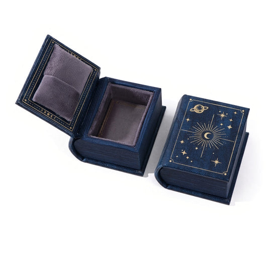 Navy book-shaped ring box with gold celestial decoration, shown open and closed